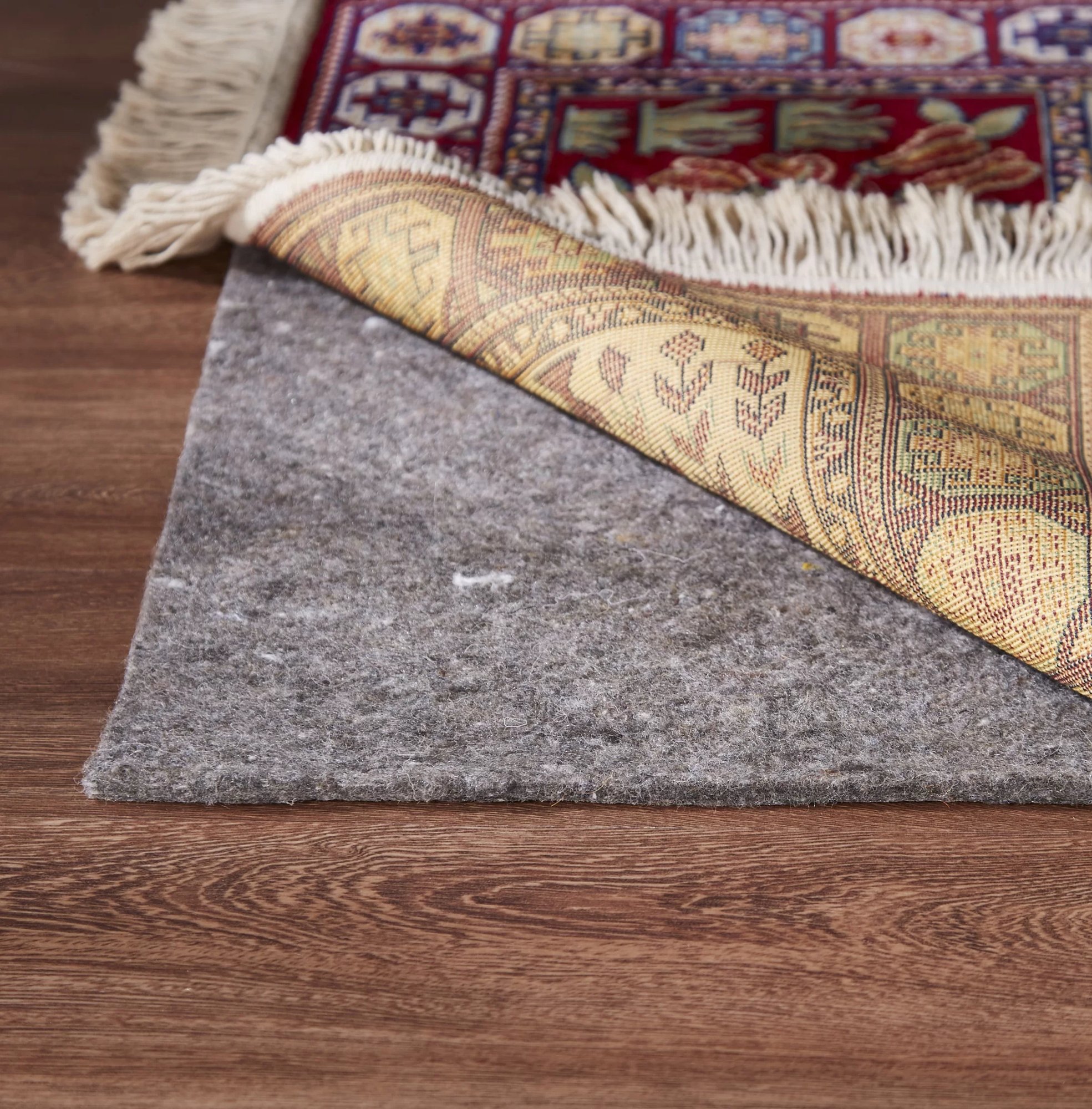 A rug pad beneath the corner of an Oriental rug on a wood floor