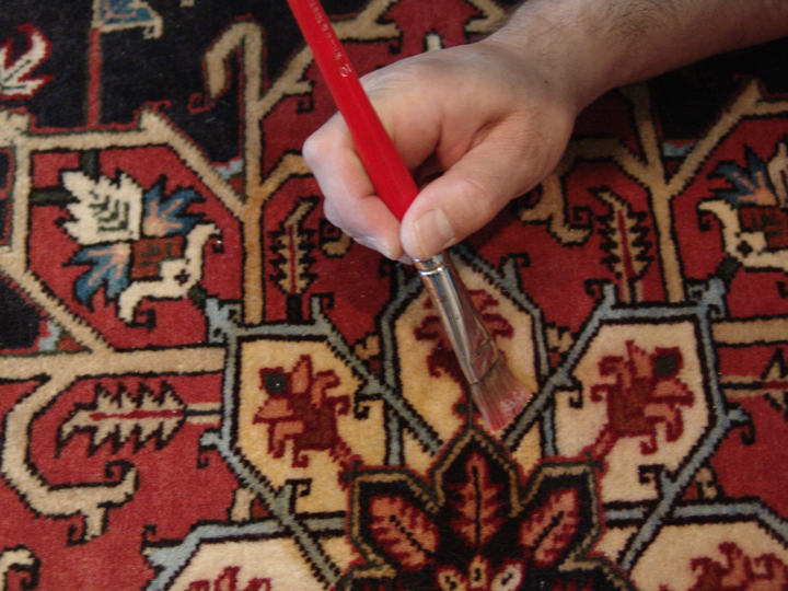 A technician hand-brushing a spotting solution into a red Oriental rug