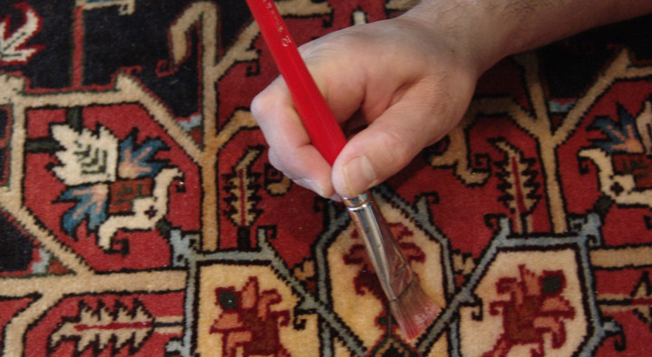 A spot on a red Oriental rug being treated with a fine applicator
